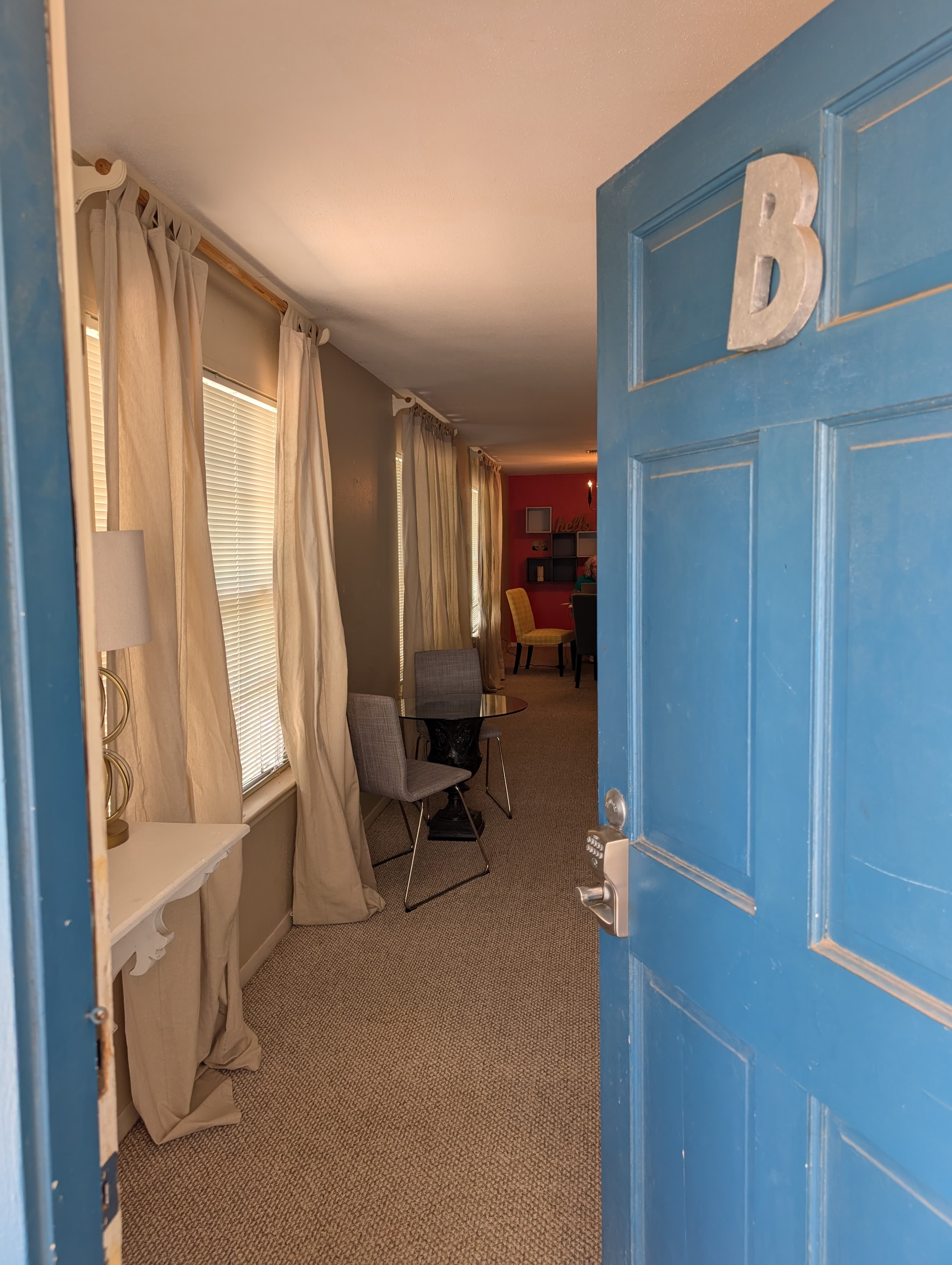 A blue door slightly ajar reveals a cozy room with chairs, curtains, and a small table.