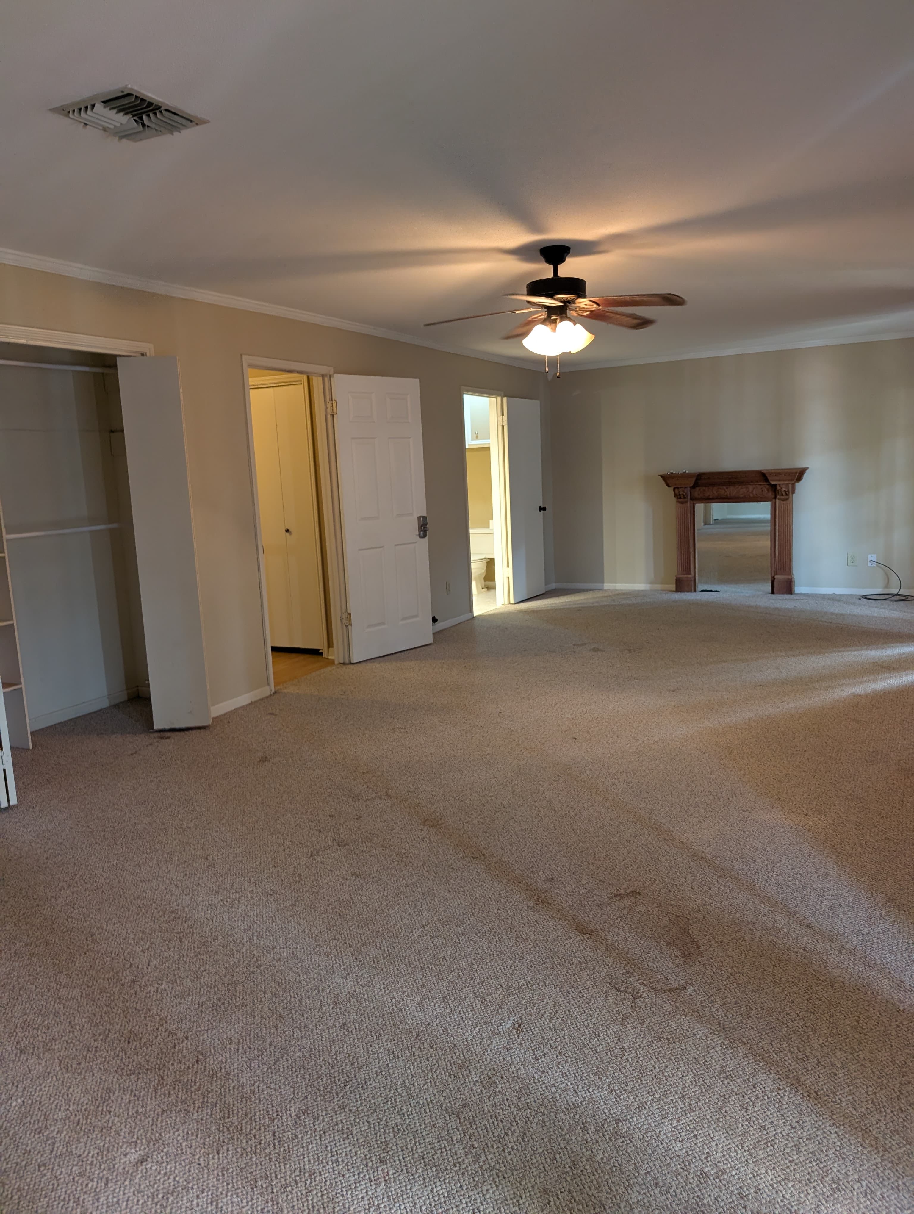 A spacious, carpeted living room with a ceiling fan and doors leading to adjacent rooms.