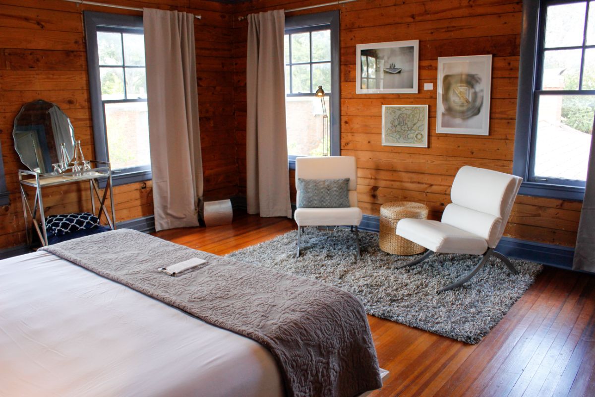 A cozy bedroom featuring a bed, a textured area rug, modern seating, and wooden walls.