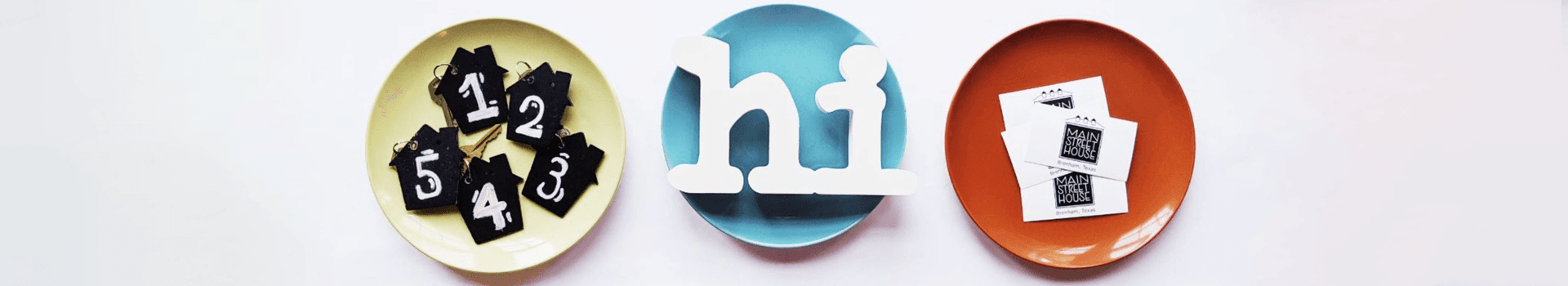 Three plates with numbered black tags, a white "hi" sign, and photo cards.