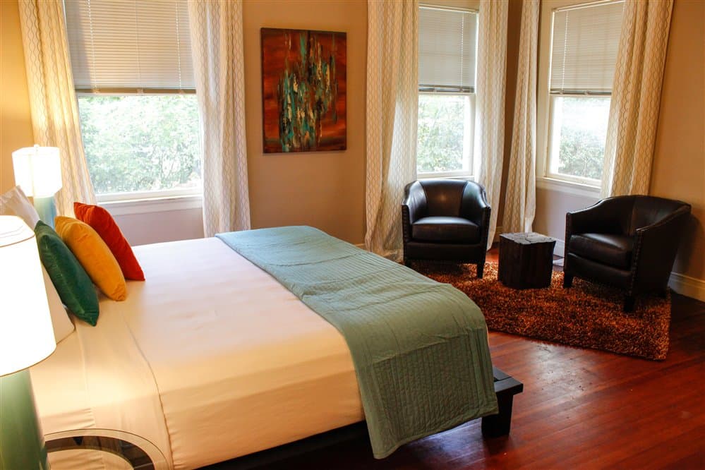 Bright, cozy bedroom with a bed, colorful pillows, and seating area by the windows.
