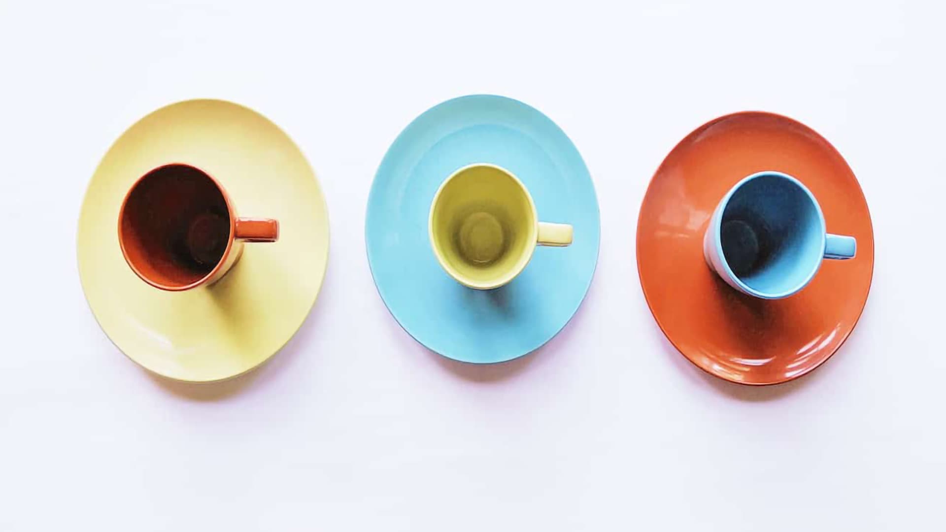 Three colorful cups on matching saucers arranged on a white background.