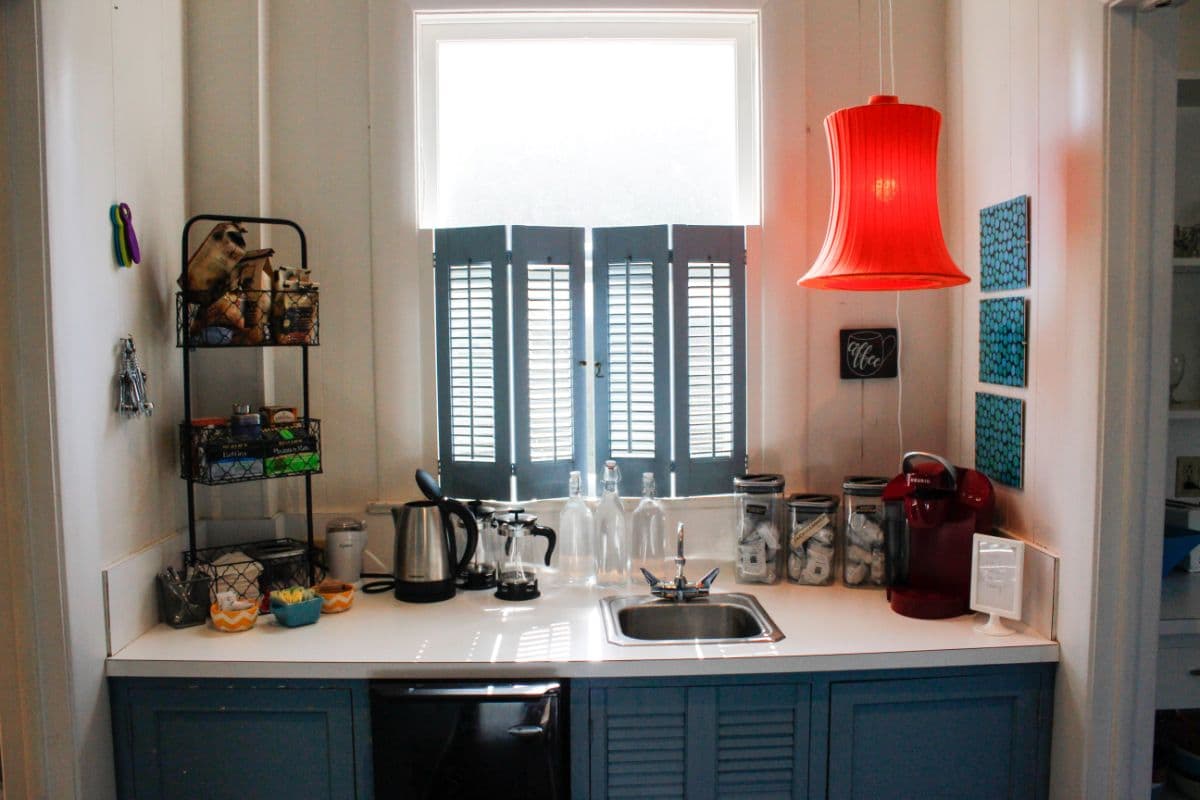A cozy kitchen corner featuring a sink, coffee maker, colorful storage jars, and a bright red pendant light.
