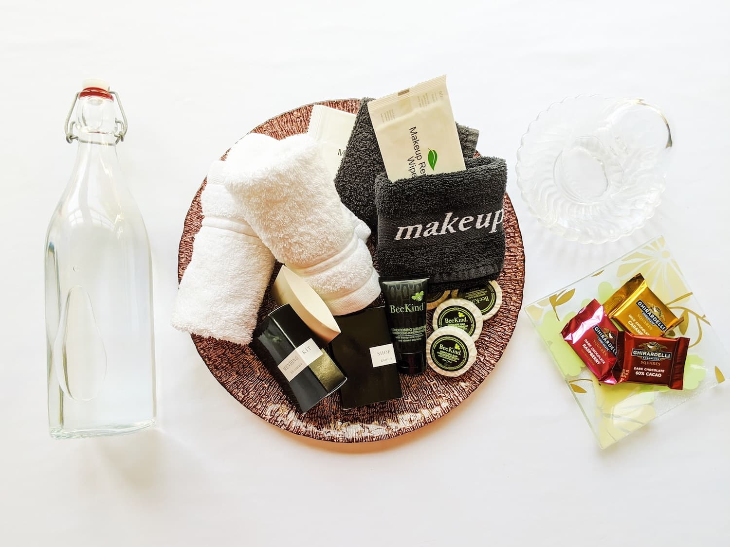 A decorative platter holds towels, skincare products, a water bottle, and various tea and sugar packets.