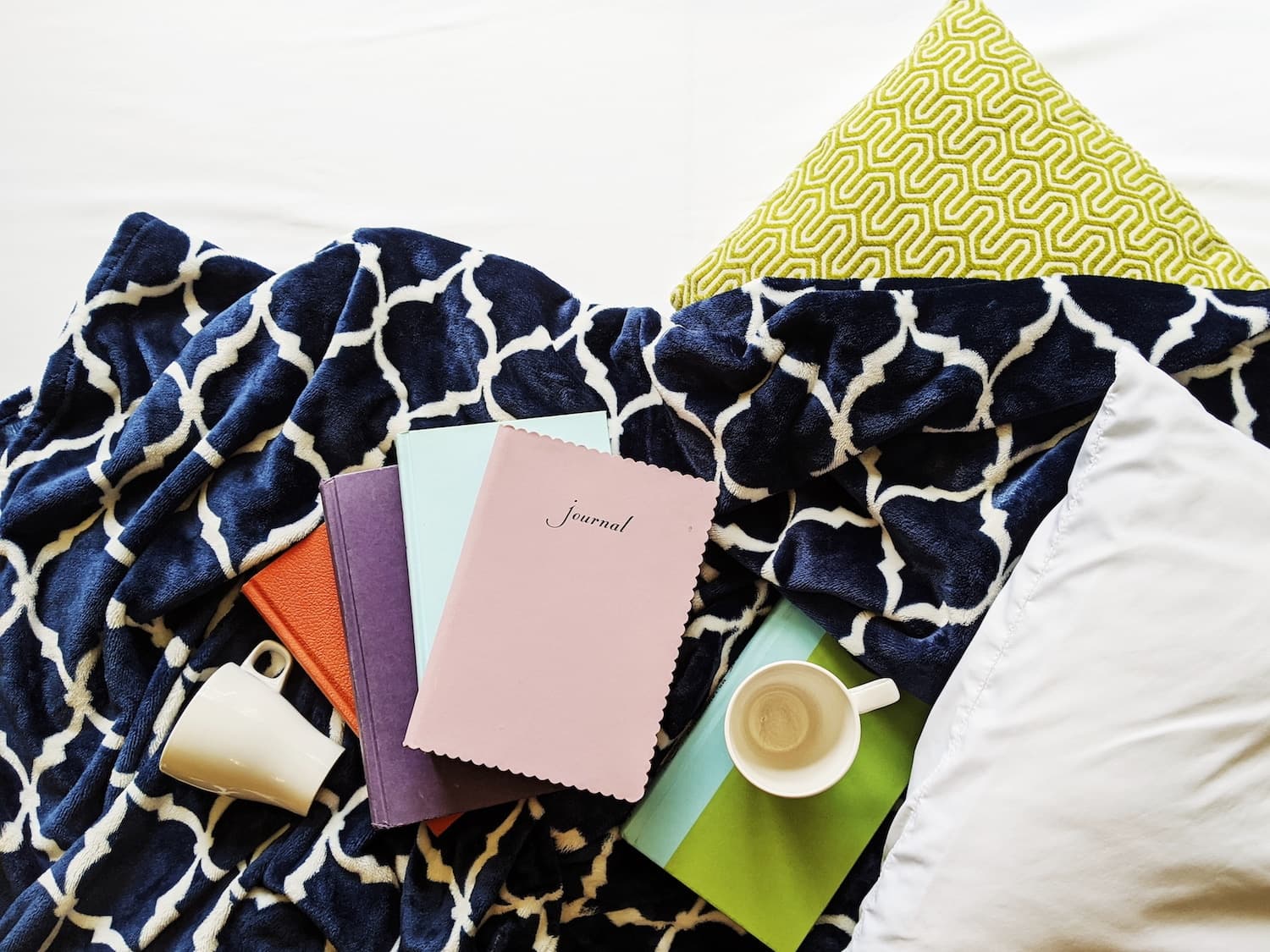 A cozy scene featuring journals, a cup, and pillows on a patterned blanket.