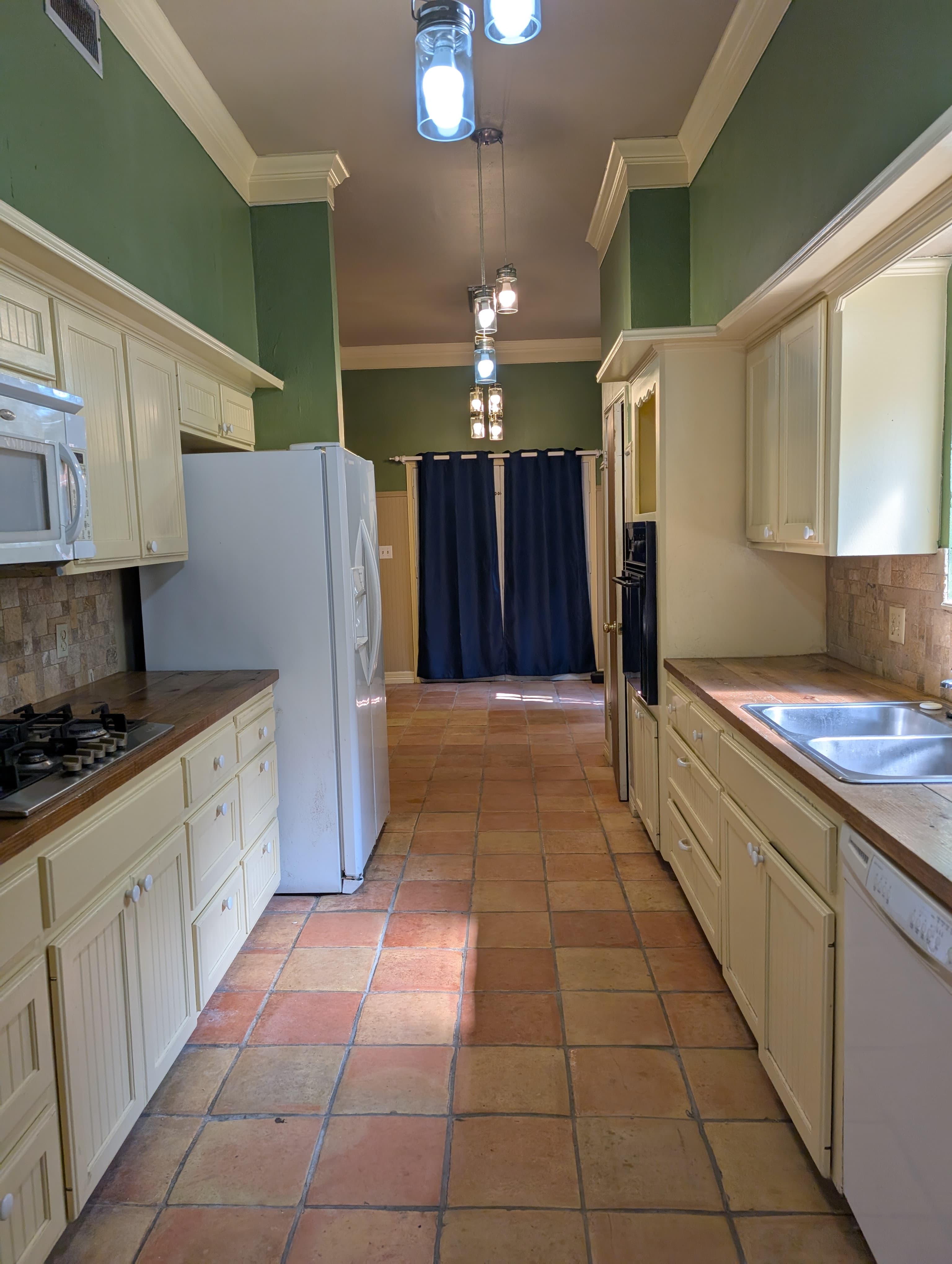 A bright kitchen with white cabinetry, a gas stove, and terracotta tiled flooring.