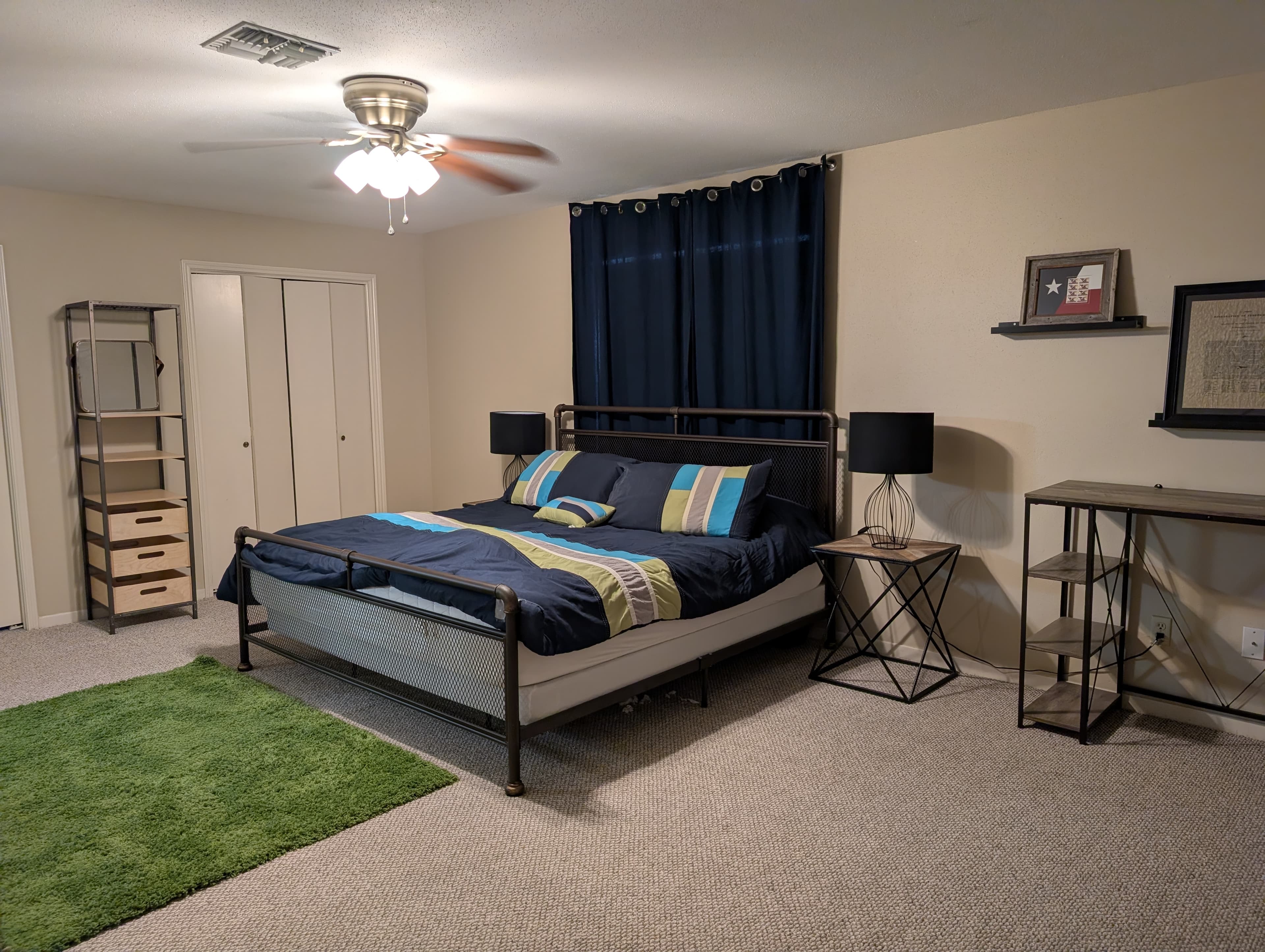 A cozy bedroom featuring a bed with blue and green bedding, a green rug, and modern furniture including a desk and shelving unit.