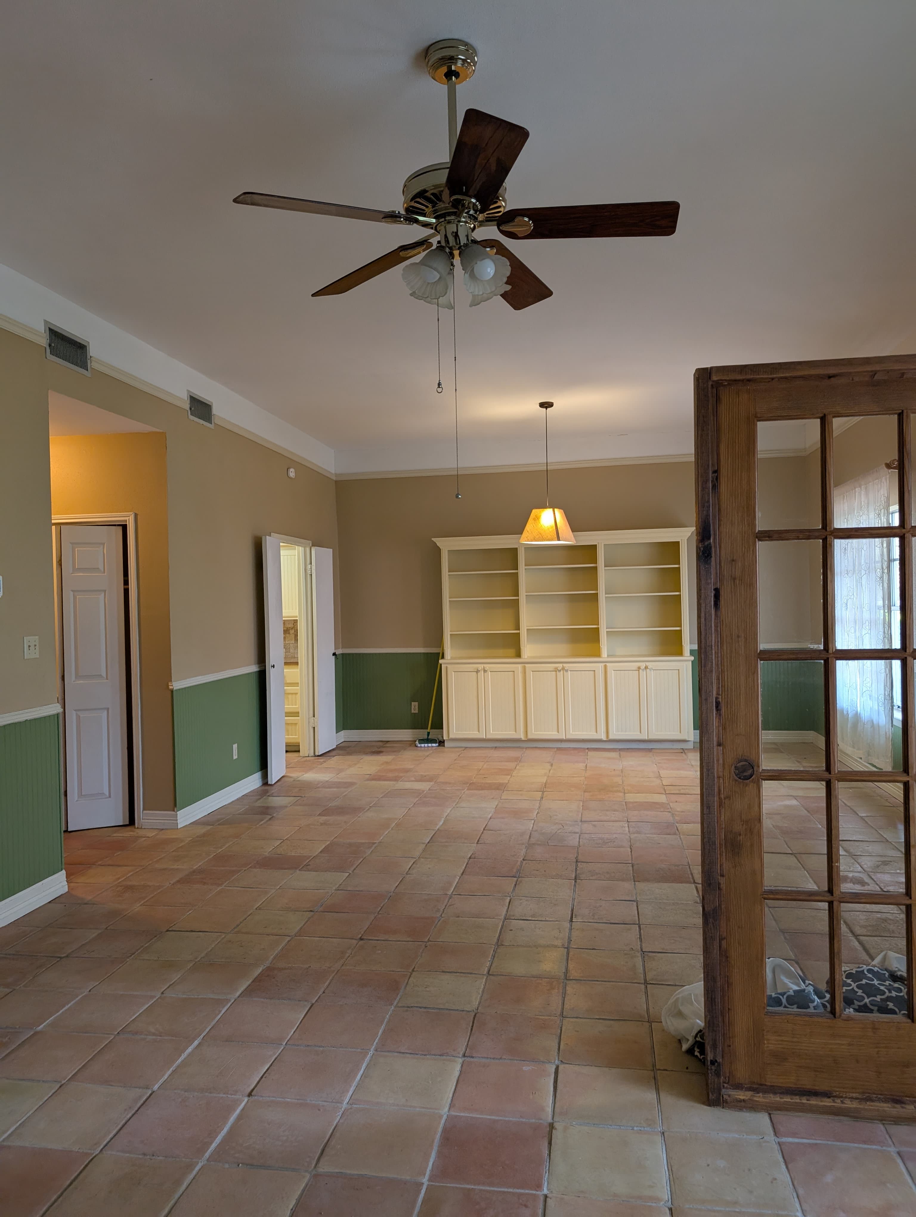 Living room with a ceiling fan, tile floor, and built-in shelves against a green and beige wall.