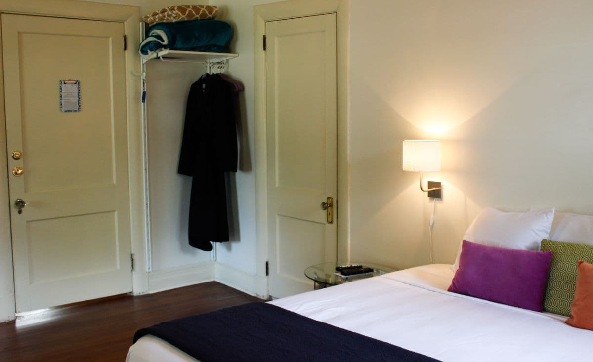A cozy bedroom featuring a bed with colorful pillows, a bedside lamp, and a closet with hanging garments.