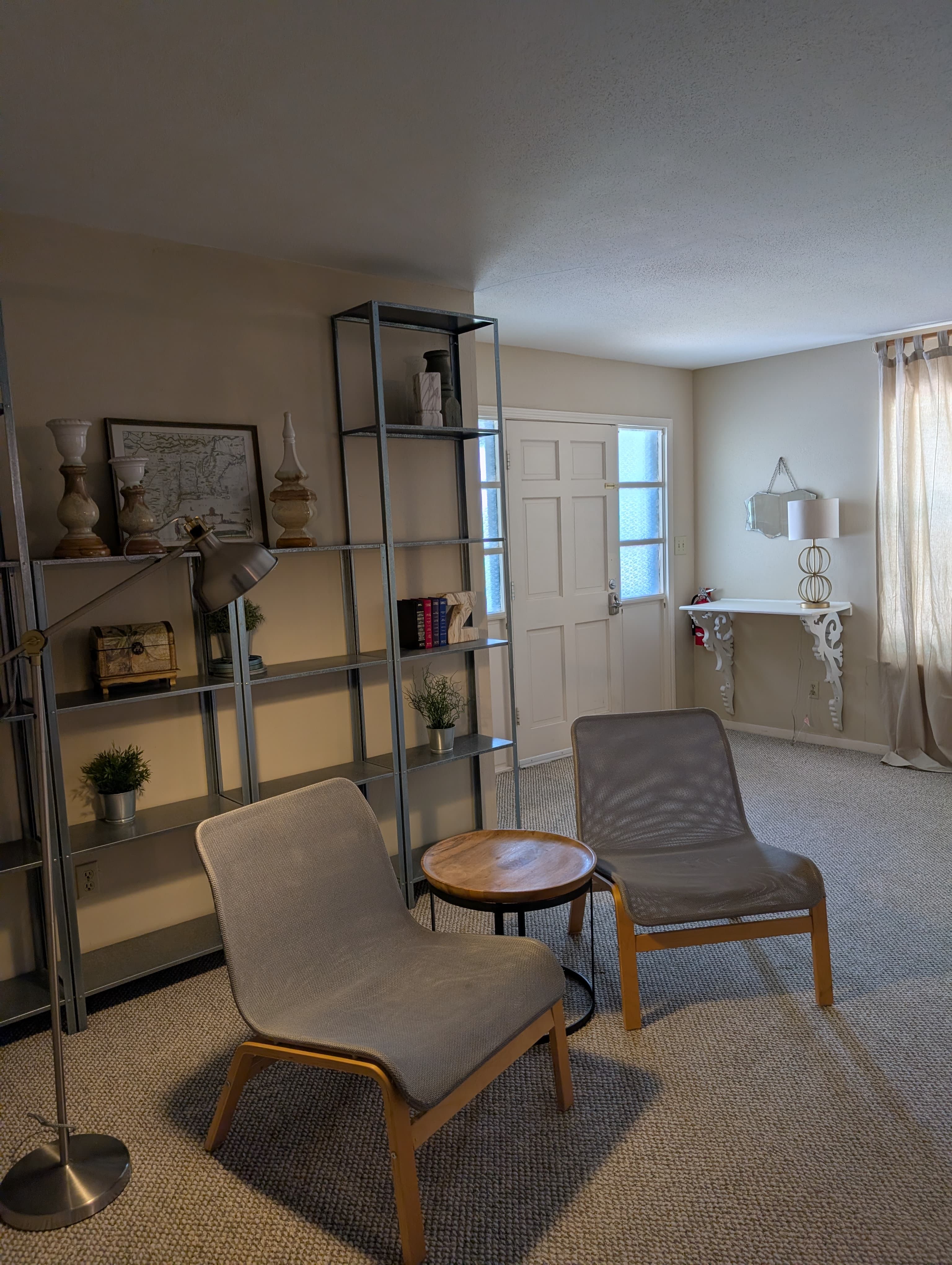 Cozy living space featuring two lounge chairs, a small table, a bookshelf, and an entryway.