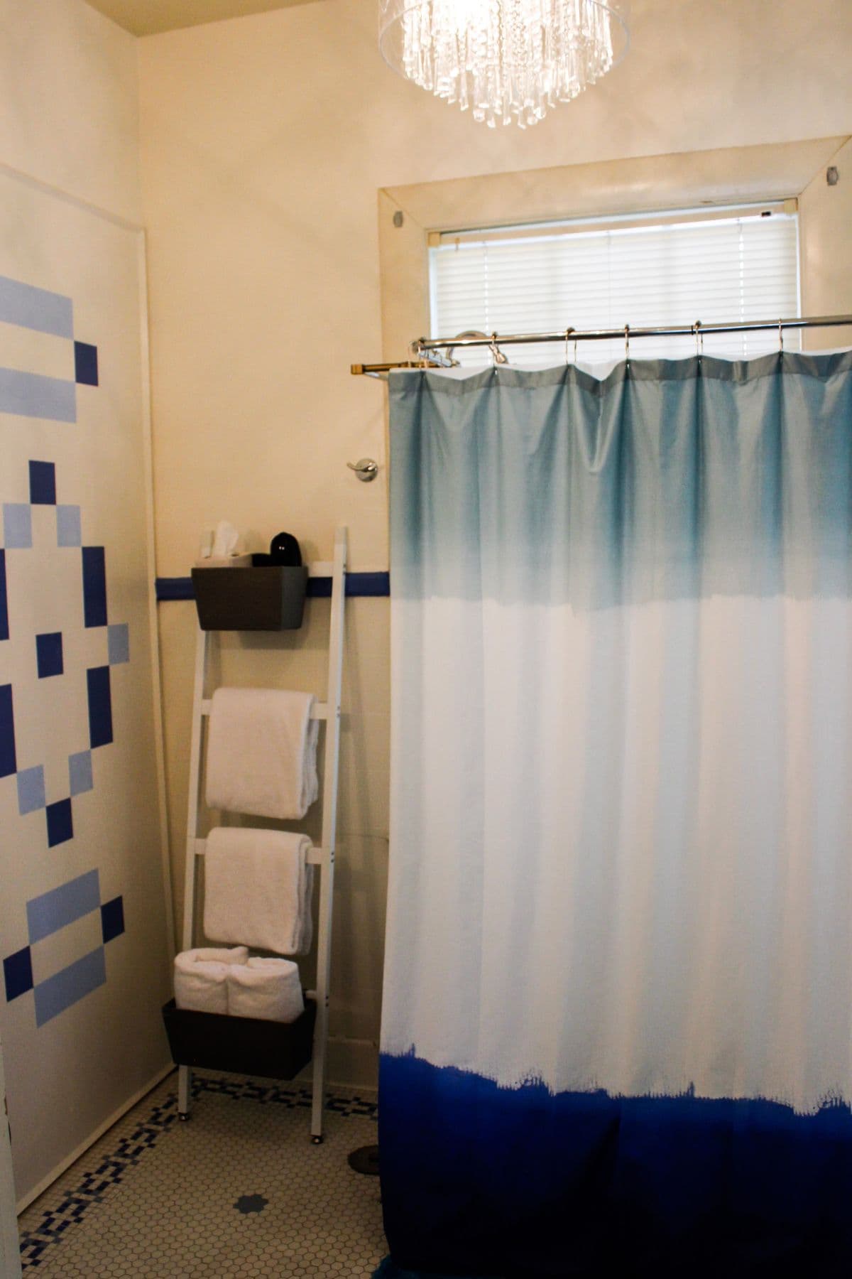 A stylish bathroom featuring a light blue ombre shower curtain, white towels, and a decorative chandelier.
