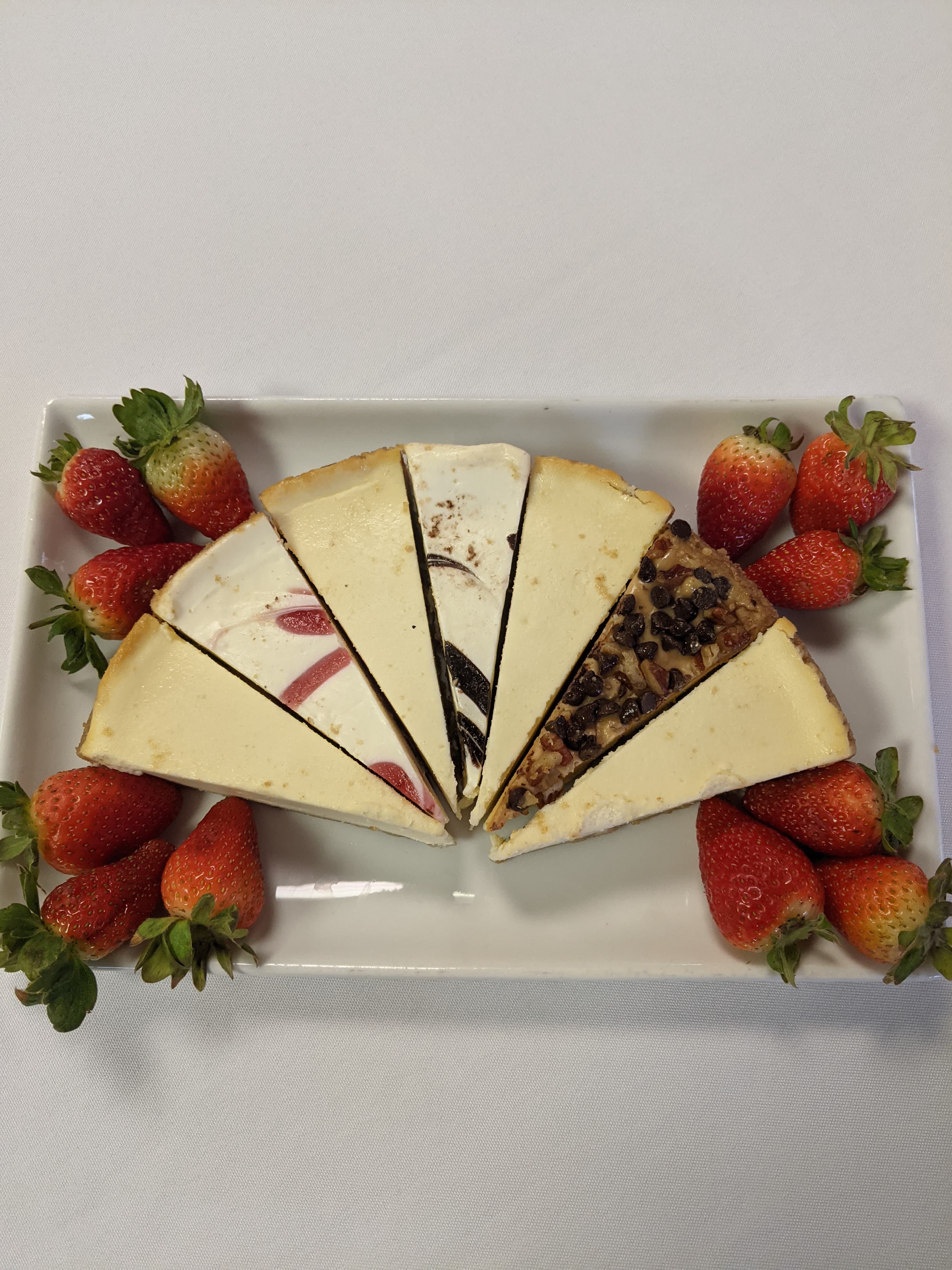 A tray featuring slices of cheesecake in various flavors, surrounded by fresh strawberries.