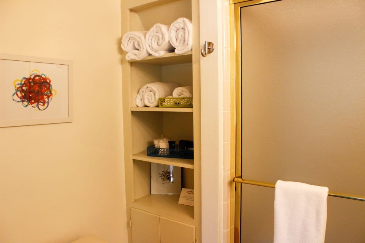 A neatly organized bathroom shelf with rolled towels, toiletries, and a glass shower door.
