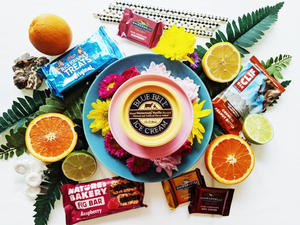 Colorful arrangement of ice cream, candies, and fresh fruits surrounded by flowers and greenery.