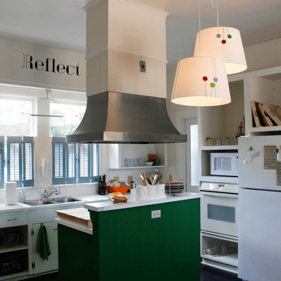 Bright and modern kitchen featuring green cabinetry, stainless steel range hood, and pendant lights.