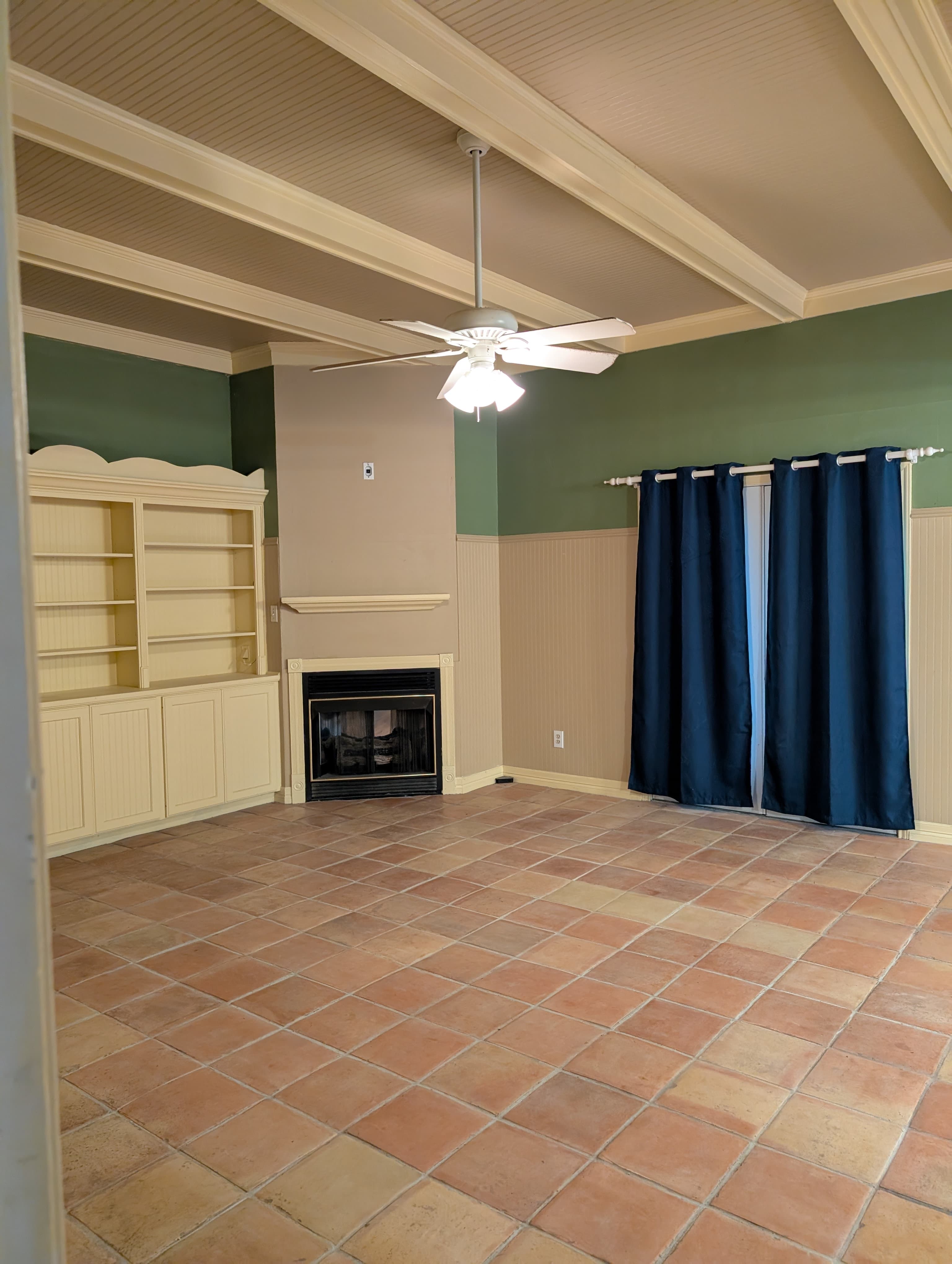 A spacious living room with tiled flooring, a fireplace, built-in shelves, and dark blue curtains.