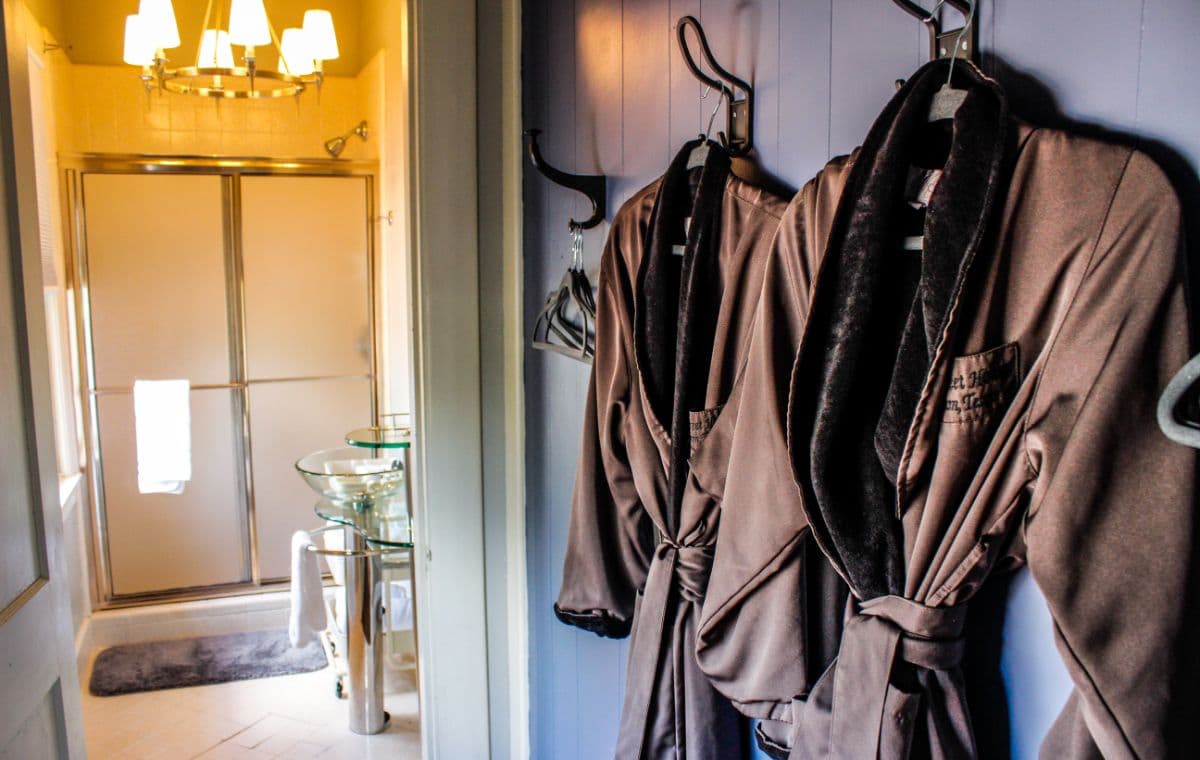 Two plush bathrobes hang on hooks in a well-lit bathroom near a glass shower.