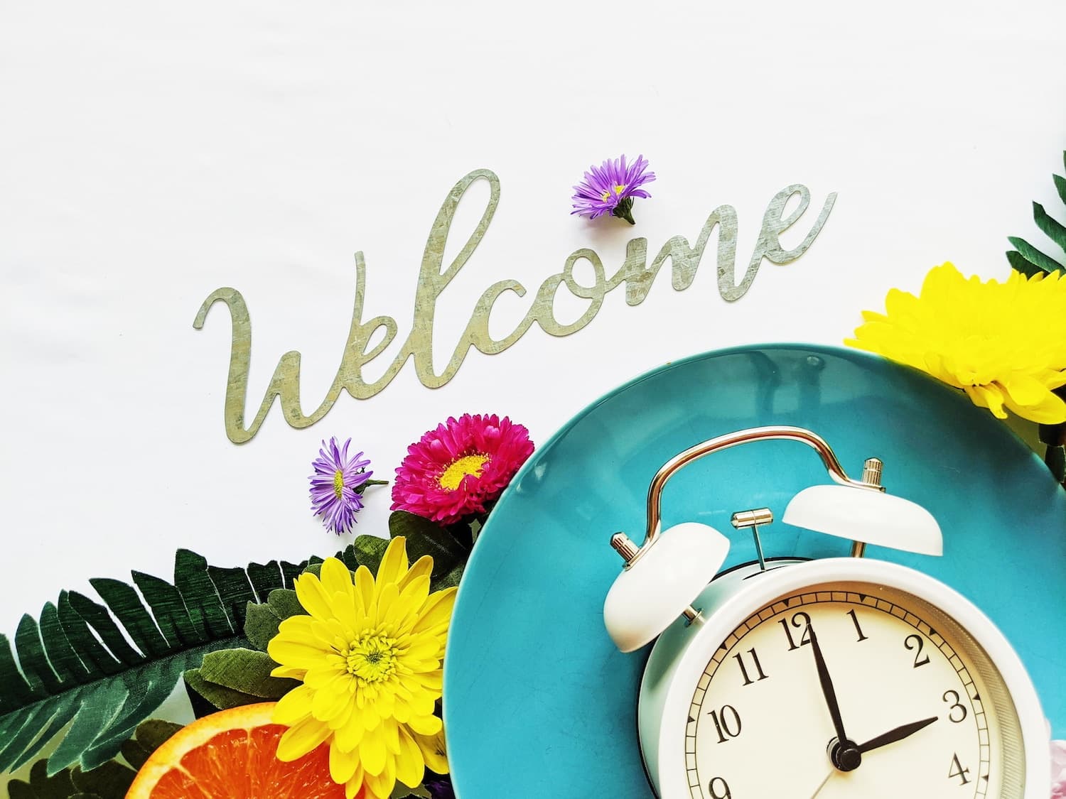 A clock sits beside a teal plate adorned with flowers and the word "Welcome" in elegant script.